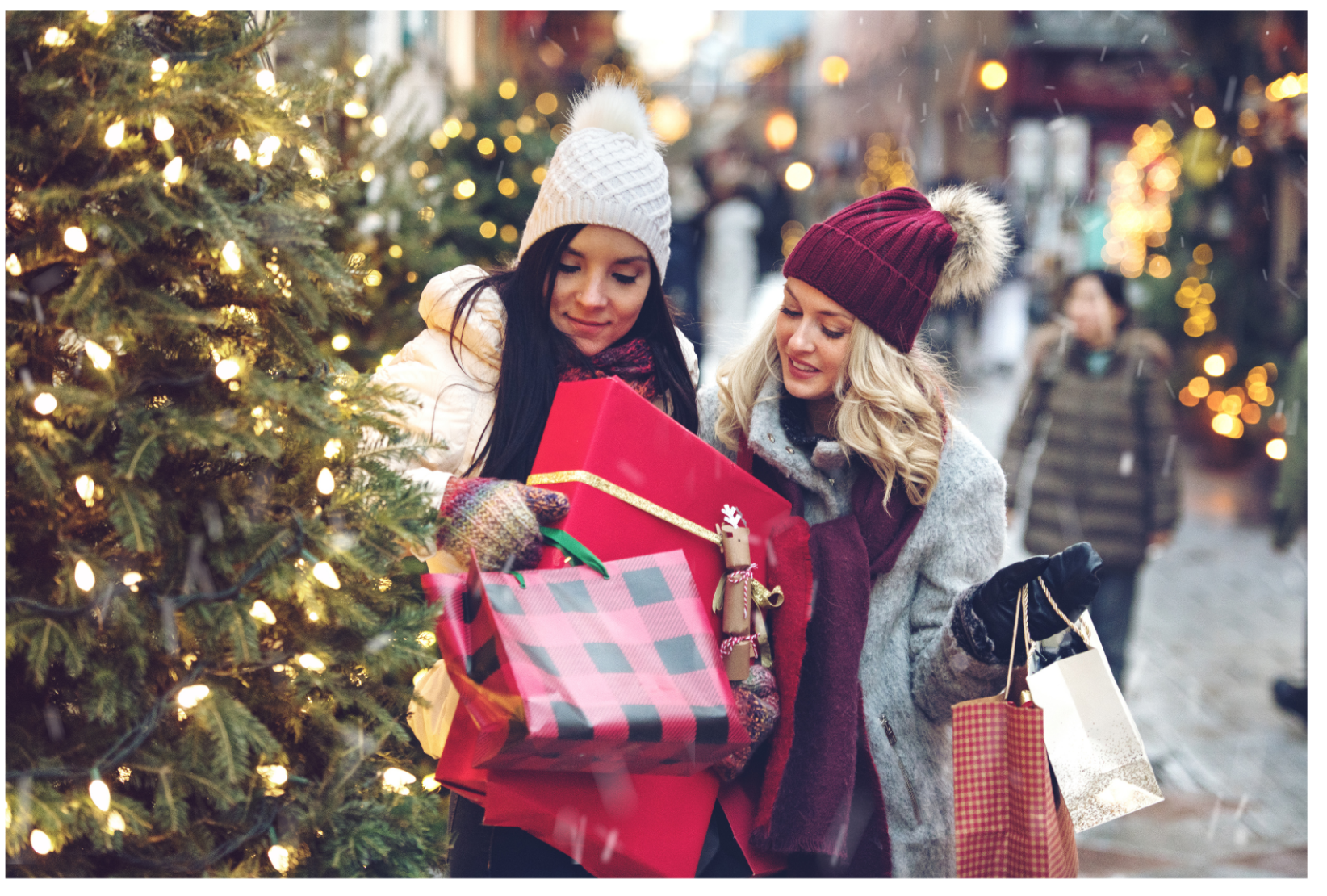 Marketing zu Weihnachten auf Instagram Zwei Frauen sind beim Einkaufen in der Weihnachtszeit unterwegs. Sie tragen Mützen und jeweils viele Einkaufstaschen aus dem lokalen Handel. Ein Weihnachtsbaum schafft Atmosphäre.